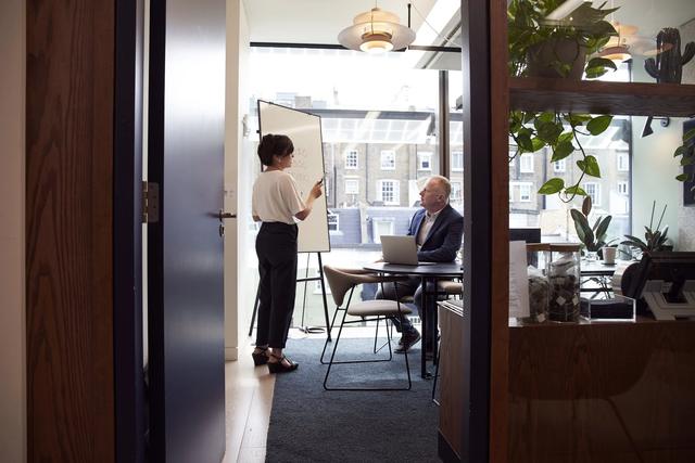 An owner and a colleague talking in a glass-walled office